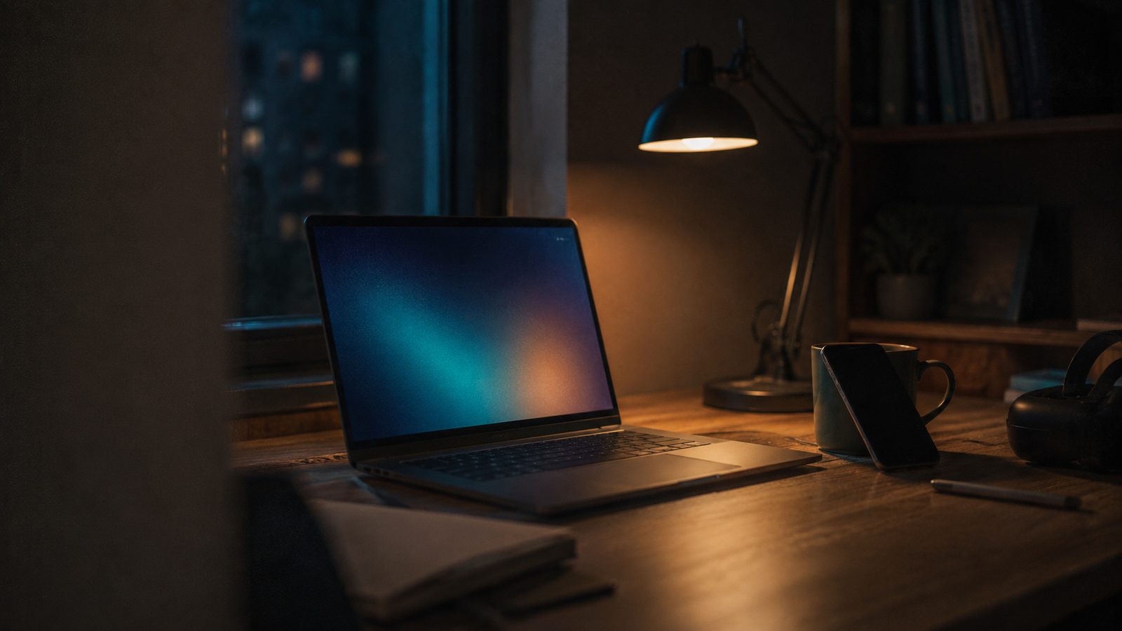 An evening desk with a laptop, phone and coffee, with the VR headset pushed to the far edge of the frame